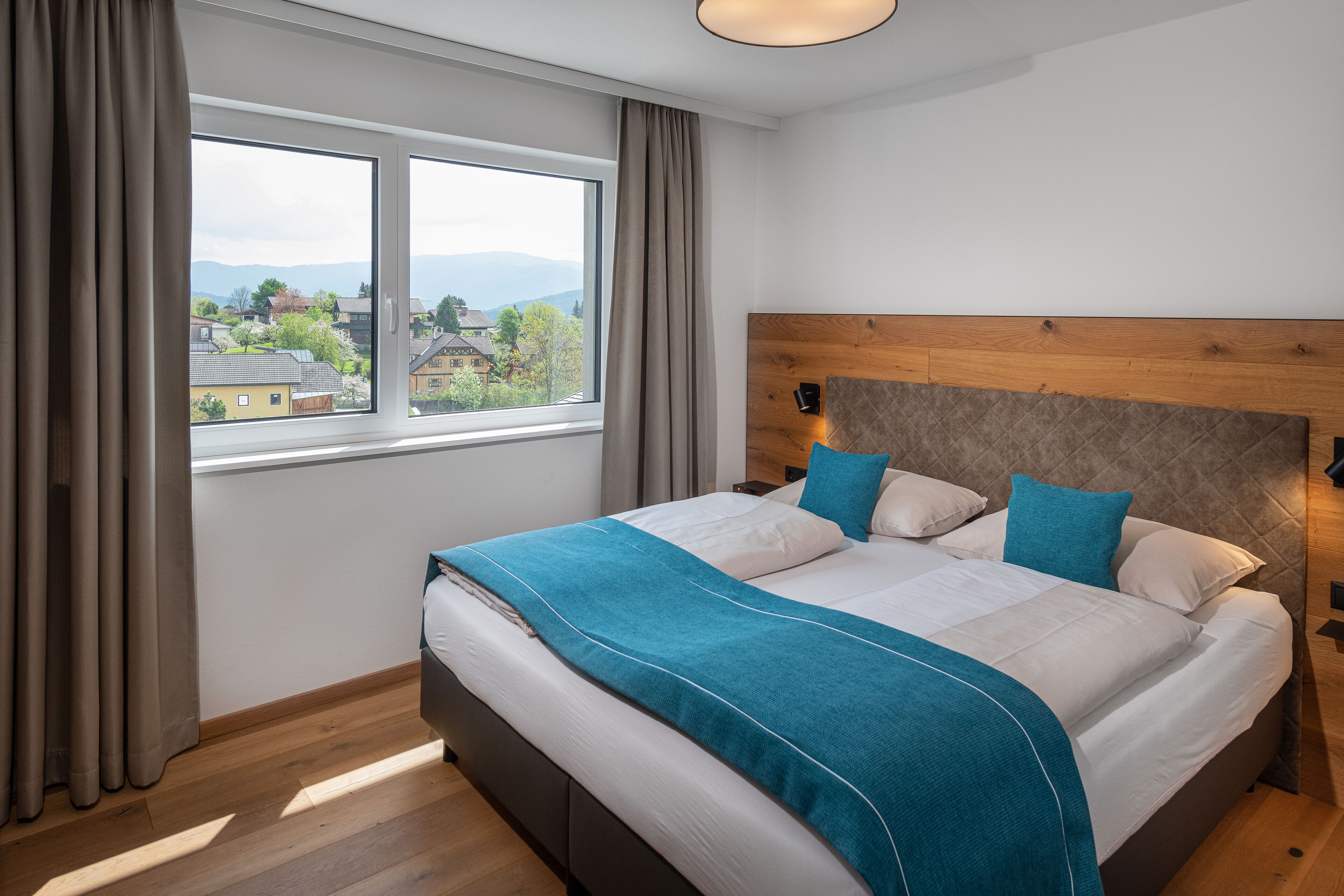 A bedroom with a large bed, a wooden headboard, and a view of a residential area through a window.