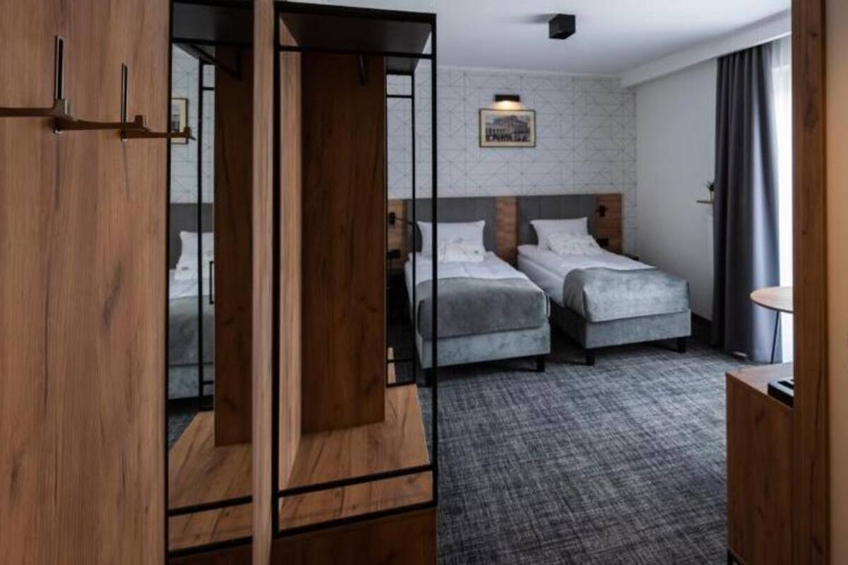 A hotel room with two beds, a wooden wardrobe, a grey carpet, and a small table.