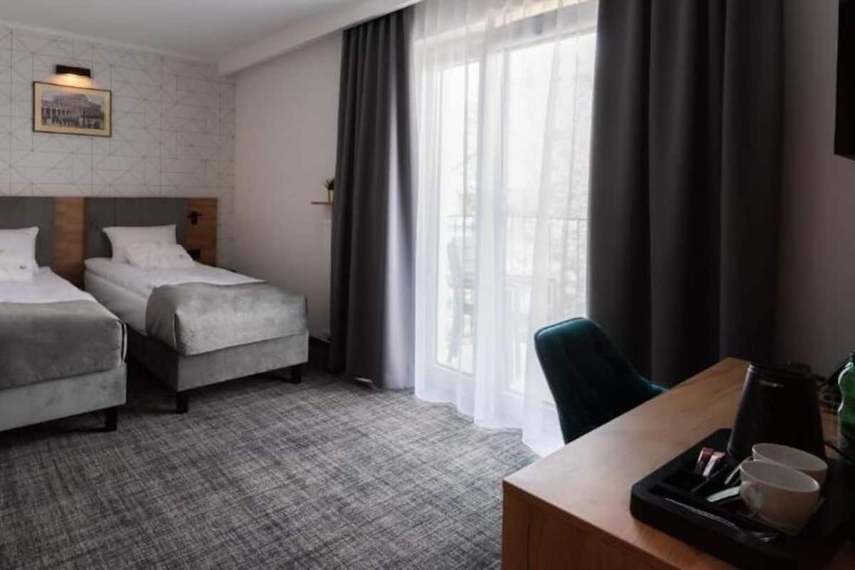 A hotel room with two beds, a desk with a tray, and a large window with curtains.