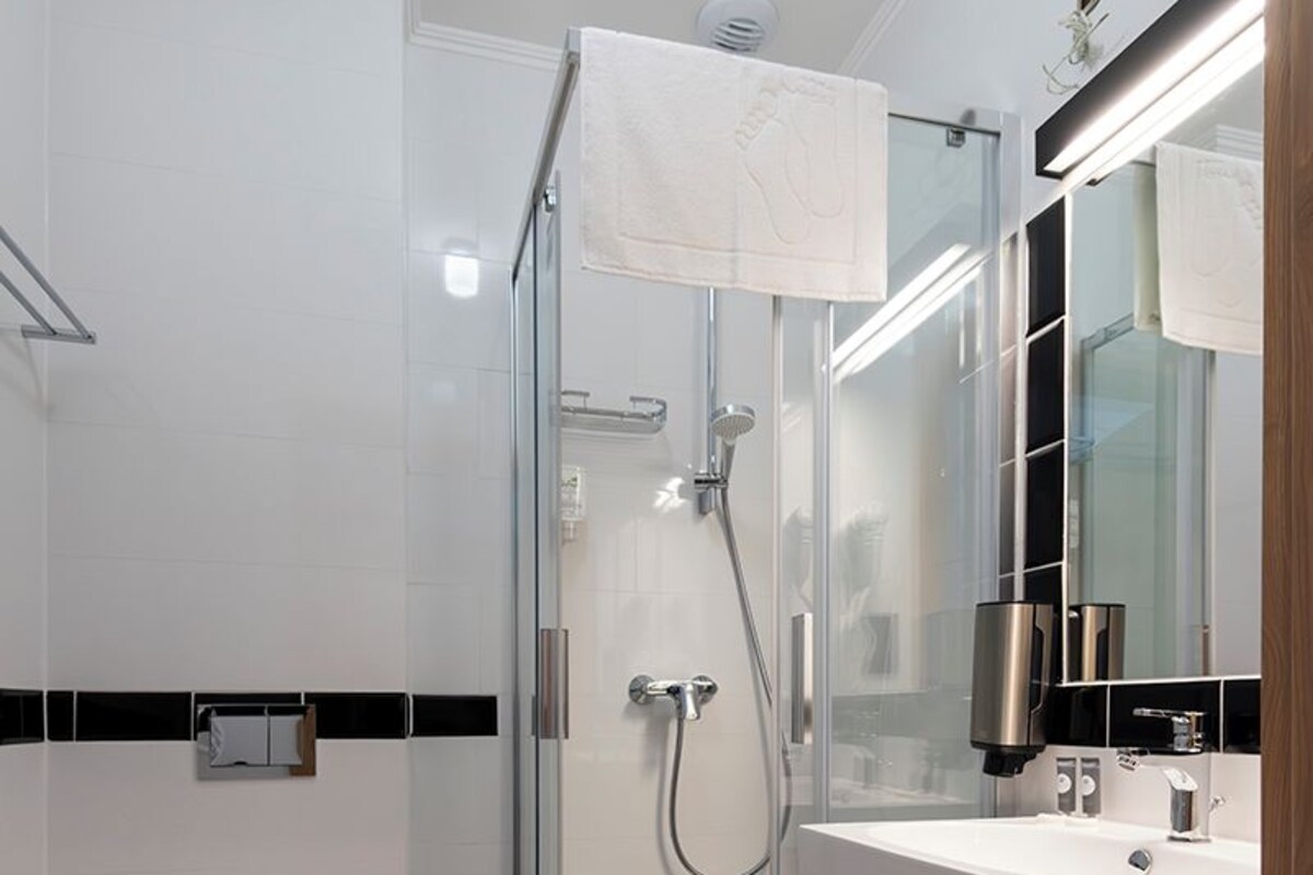 A modern bathroom with a glass-enclosed shower, a white sink with a mirror, and a black and white checkered floor.