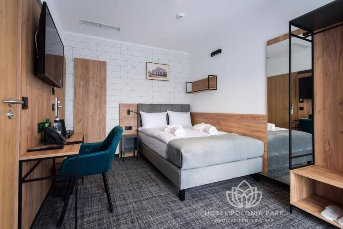 A hotel room with a bed, a desk, a chair, a TV, and a mirror.