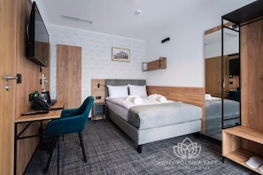A hotel room with a bed, a desk, a chair, a TV, and a mirror. - Polonia Park Medical Center & SPA (Busko-Zdroj)