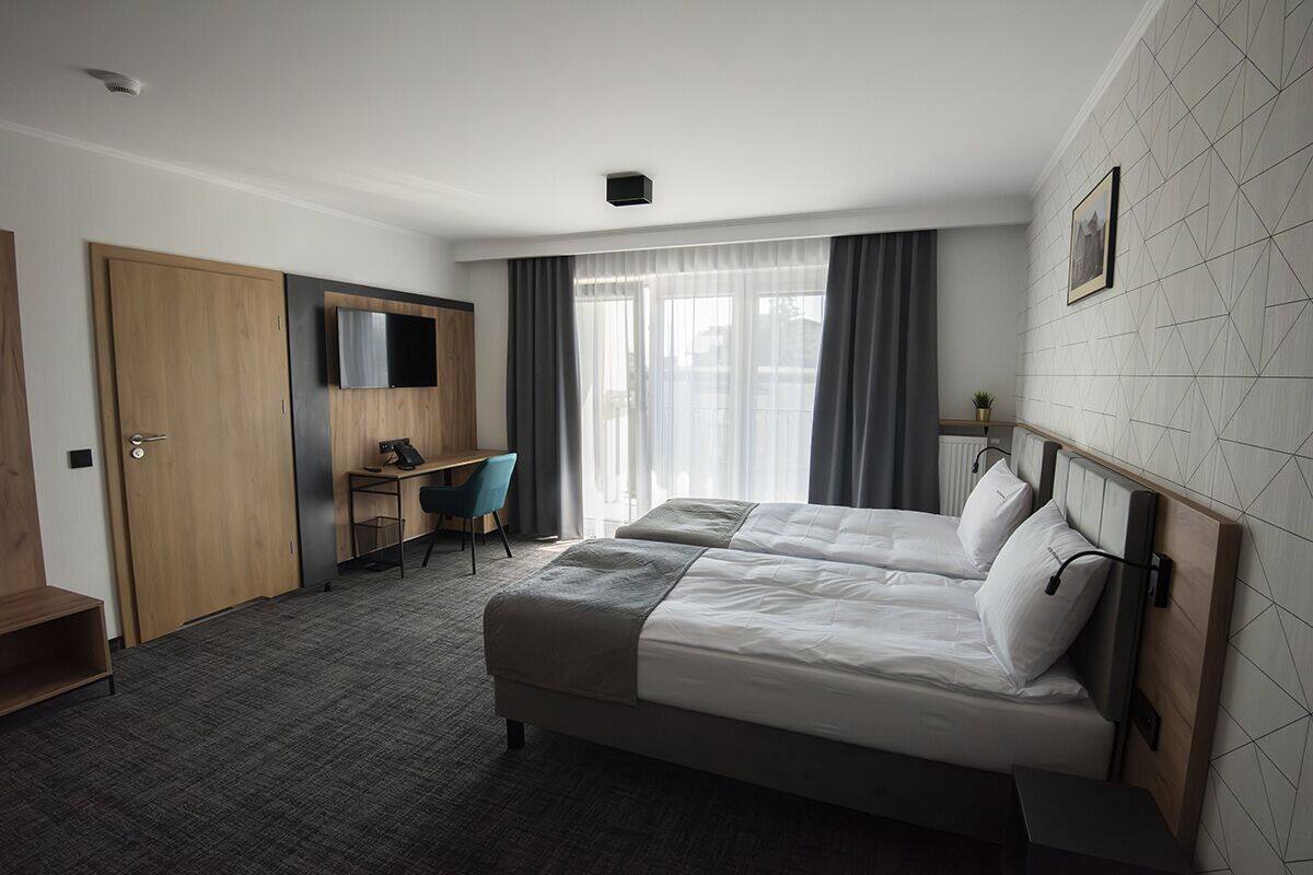A hotel room with a bed, a desk, a chair, a TV, and a window with curtains.