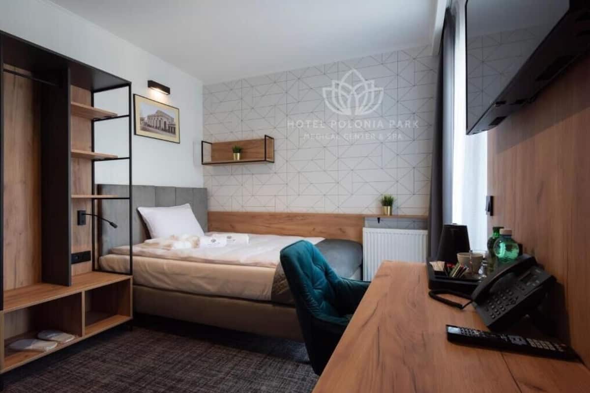 A hotel room with a bed, a desk with a phone, a shelf with a plant, and a picture on the wall.