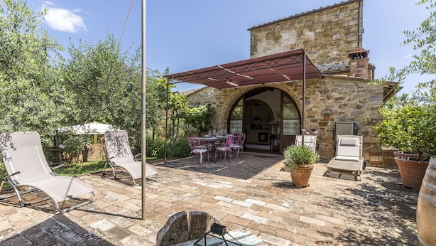 Ein Steinhaus mit einer Terrassenanlage, die Außenmöbel, eine Pergola und Kübelpflanzen umfasst.