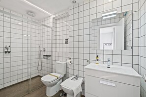 Een moderne badkamer met witte tegels, een toilet, een bidet, een wastafel en een spiegel.