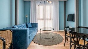 Ein modernes Wohnzimmer mit einem blauen Sofa, einem runden Glastisch und einem Essbereich mit Stühlen.
