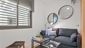 Ett modernt vardagsrum med en grå soffa, två runda speglar, ett litet bord med en växt och en träbänk.