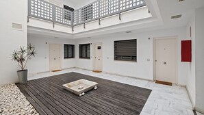 En rymlig innergård med ett trädäck, en central sittgrupp och ett högt tak med takfönster.