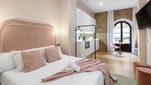 Un dormitorio moderno con una cama grande, una kitchenette y vistas de la ciudad a través de un amplio ventanal de arco.