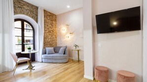 Una sala moderna con pared de piedra, un sofá gris, un sillón rosa, una mesita redonda y un televisor montado en la pared.