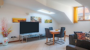 A modern living room with a flat-screen TV, a dining table with chairs, a sofa, and a decorative vase with flowers. - BnButler - Asiago 41 (Milan)