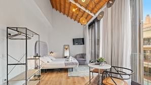 Ein modernes Hotelzimmer mit einem Bett, einer Sitzecke mit Tisch und Stühlen, einem Fernseher und großen Fenstern mit Blick auf die Stadt.