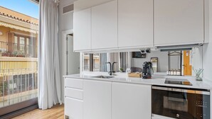 Eine moderne Küche mit weißen Schränken, einem eingebauten Backofen und einem Fenster mit Blick auf einen Balkon.