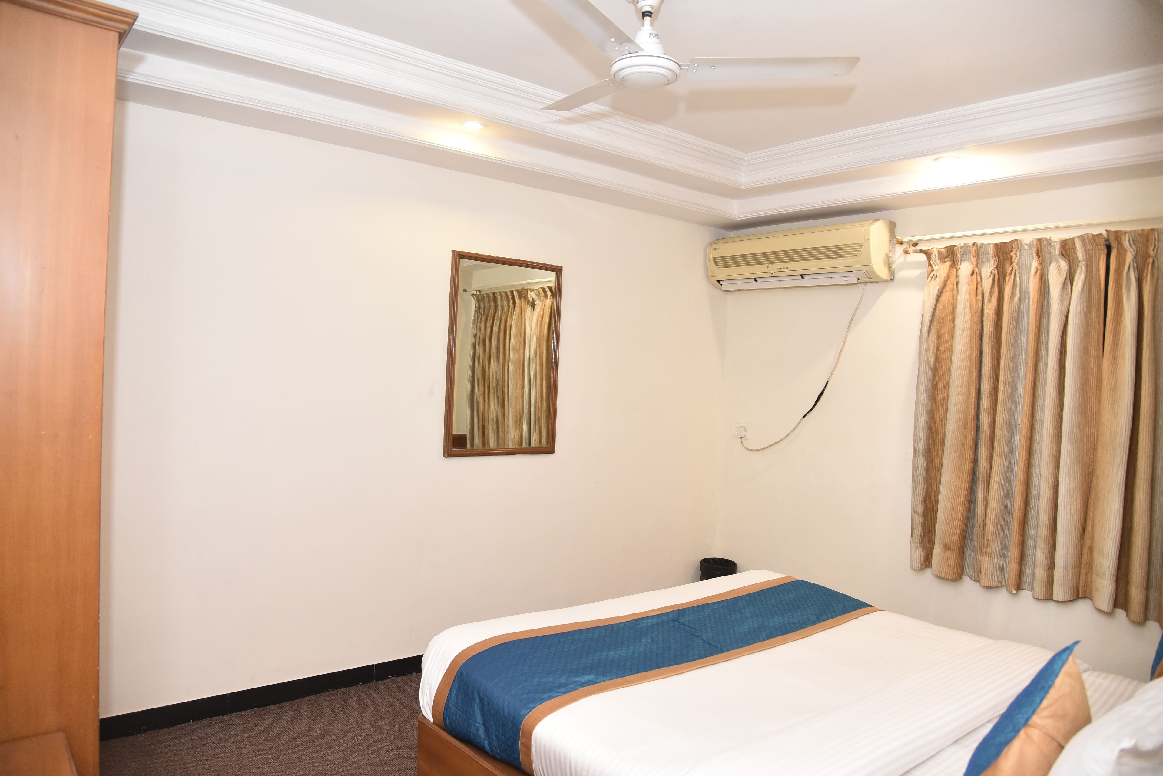 Ein Hotelzimmer mit Bett, Deckenventilator, Klimaanlage, Spiegel und Vorhängen.