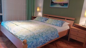 En pænt redt seng med mønstret sengetøj, et natbord med en lampe, og et billede på væggen.