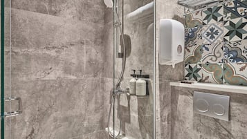 A shower with a handheld showerhead, a glass door, and a tiled wall with a geometric pattern.