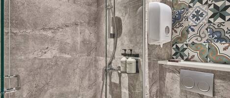 A shower with a handheld showerhead, a glass door, and a tiled wall with a geometric pattern.
