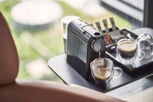 A coffee machine on a tray with two glasses of coffee, a glass of water, and a small bottle, likely containing condiments or syrups.