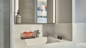 A modern bathroom with a white sink, a mirror, and a bottle of hand and body wash. - Mercure ICON Singapore City Centre (Singapore)
