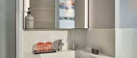 Un baño moderno con un lavabo blanco, un espejo y una botella de jabón para manos y cuerpo.