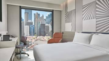 Habitación de hotel con una cama grande, un escritorio y una silla. Ofrece vistas a la ciudad a través de un ventanal.