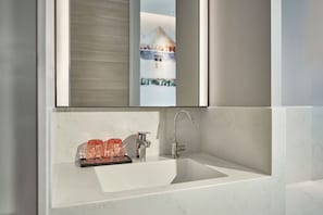 Ein Badezimmer mit einem weißen Waschbecken, einem modernen Wasserhahn und einem Glasgefäß.