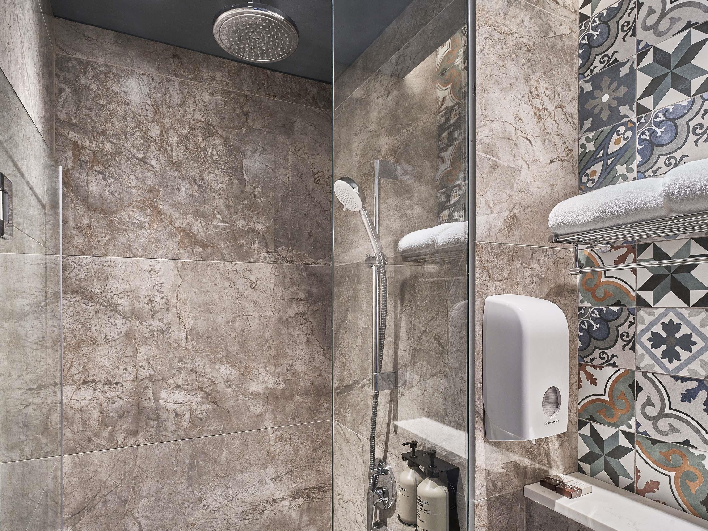 A modern bathroom with a glass-enclosed shower, marble walls, and a decorative tile backsplash.