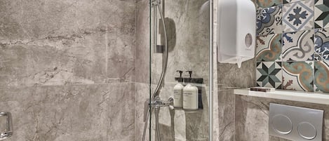 A modern bathroom with a glass-enclosed shower, marble walls, and a tiled backsplash.