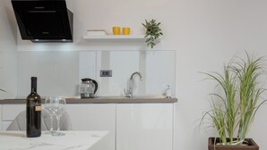 Een moderne keuken met witte kastjes, een zwarte afzuigkap, een koffiezetapparaat en een potplant.