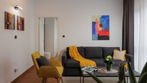 Een moderne woonkamer met een bank, een gele fauteuil, een bijzettafeltje met een tijdschrift en een plant.