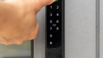 A hand pressing a button on a numeric keypad door lock.