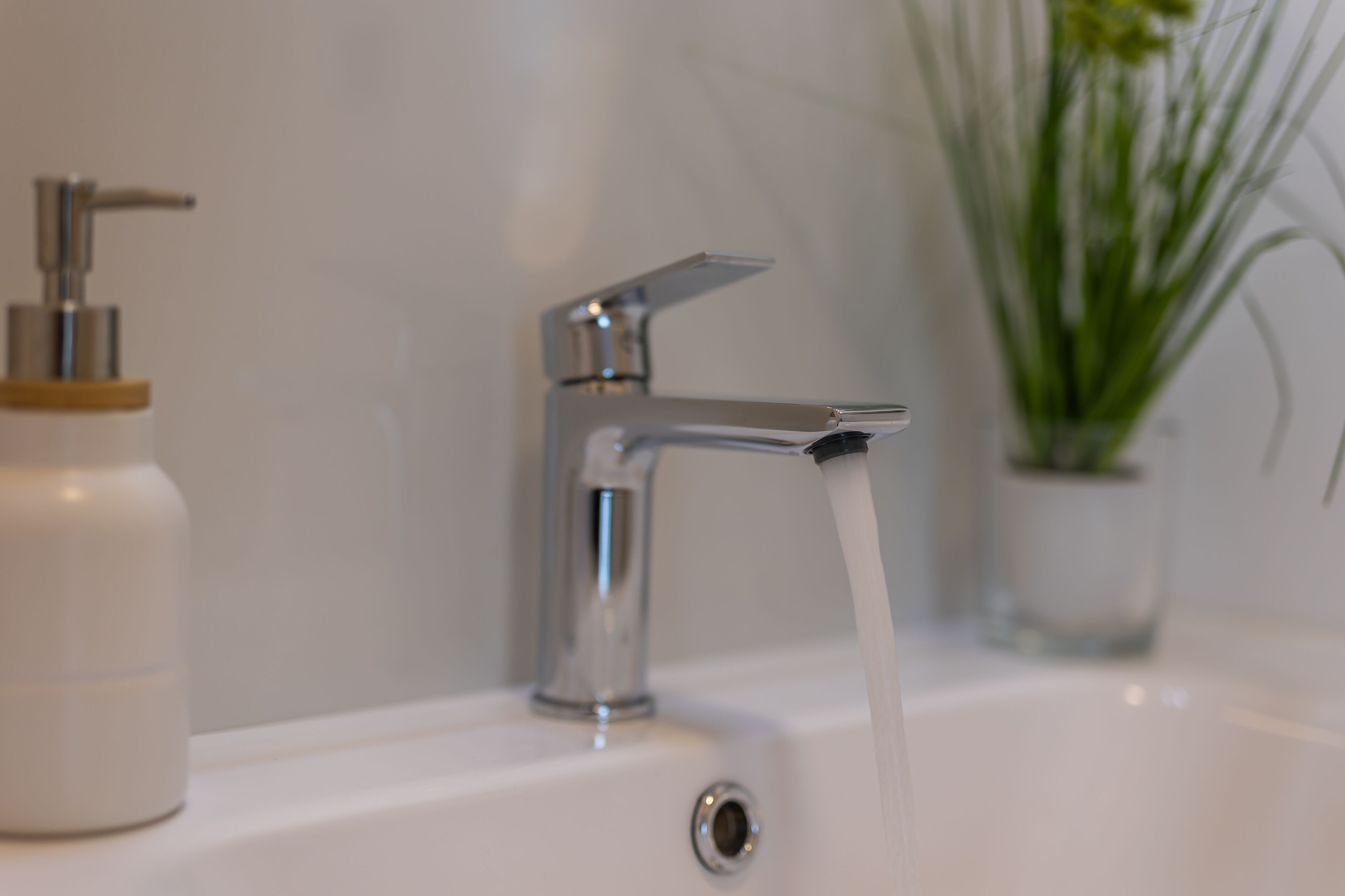 A bathroom with a modern faucet and a plant in the background.