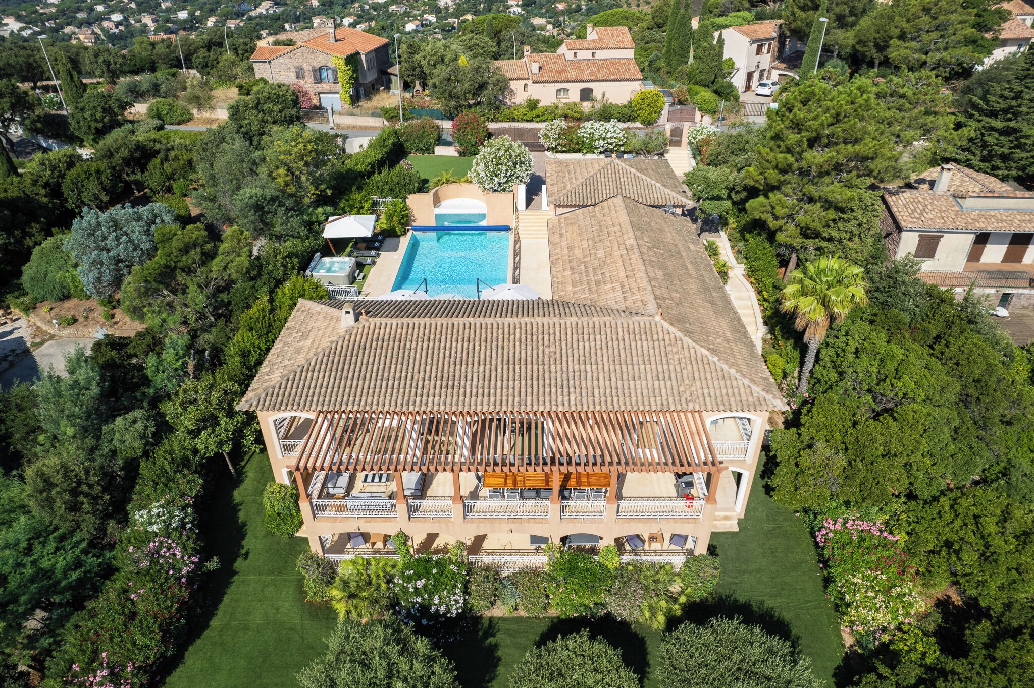 Eine Vogelperspektive zeigt eine Villa mit Swimmingpool, umgeben von üppiger Vegetation und weiteren Wohnhäusern.