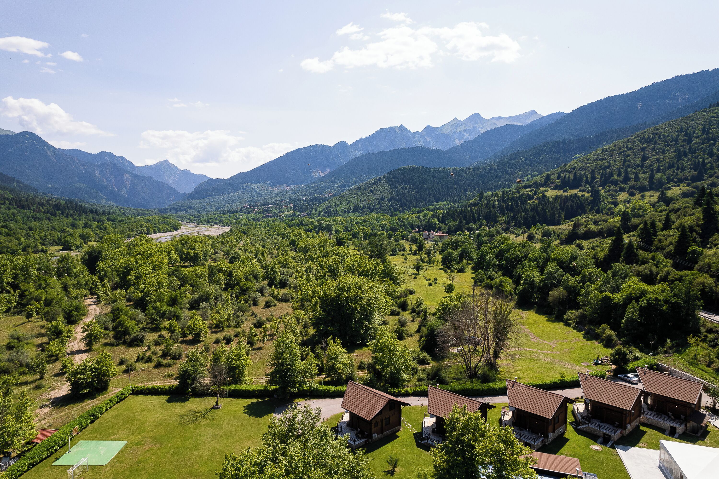 Un chalet de montagne doté de plusieurs cabanes, entouré d’une végétation luxuriante et de montagnes.