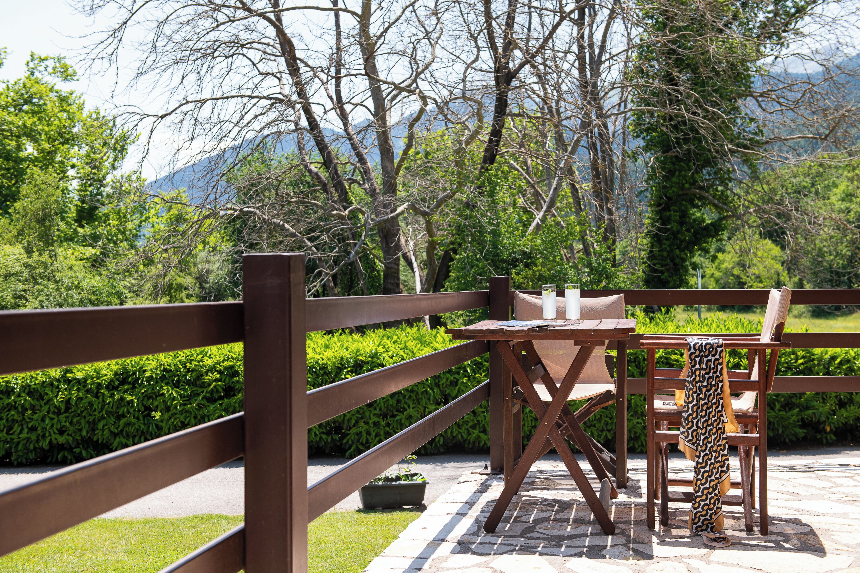 A wooden outdoor seating area with a table and chairs, surrounded by a wooden fence and greenery.