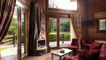 A log cabin interior with a stone fireplace, large windows, and a red upholstered sofa.
