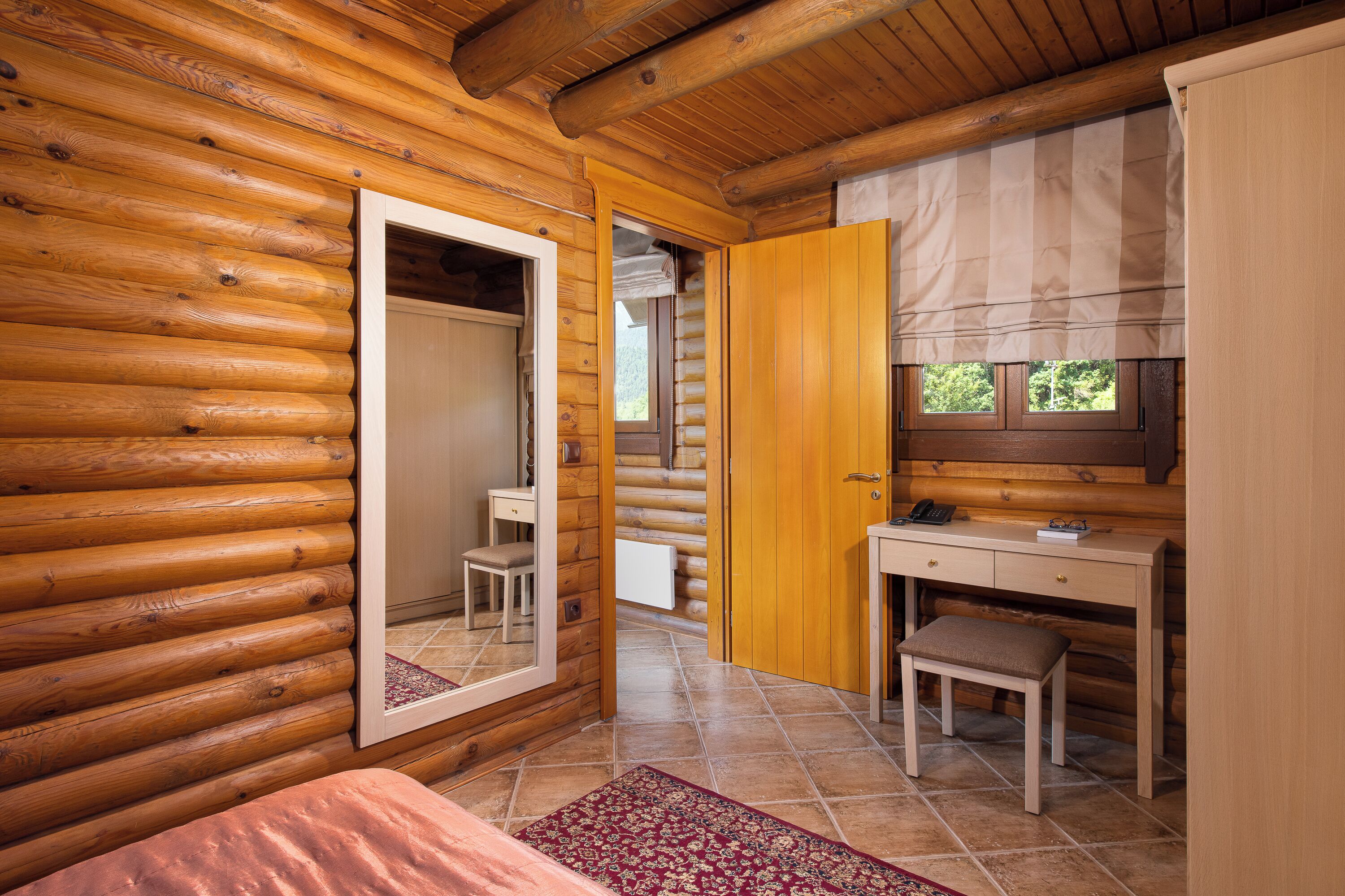 Een slaapkamer in een blokhut met een houten bureau, een stoel, een bed en een grote spiegel.