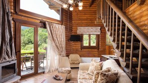 A log cabin interior with a wooden staircase, a sofa, a television, and a fireplace. - Natura Chalets (Karpenisi)