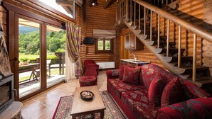 A log cabin interior with a wooden staircase, a red sofa, a fireplace, and a view of the outdoors. - Natura Chalets (Karpenisi)