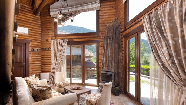 A log cabin interior with a sofa, armchair, and fireplace. - Natura Chalets (Karpenisi)