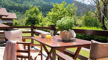A wooden table and chairs set outdoors with a mountain view, a glass of orange juice, and a potted plant.