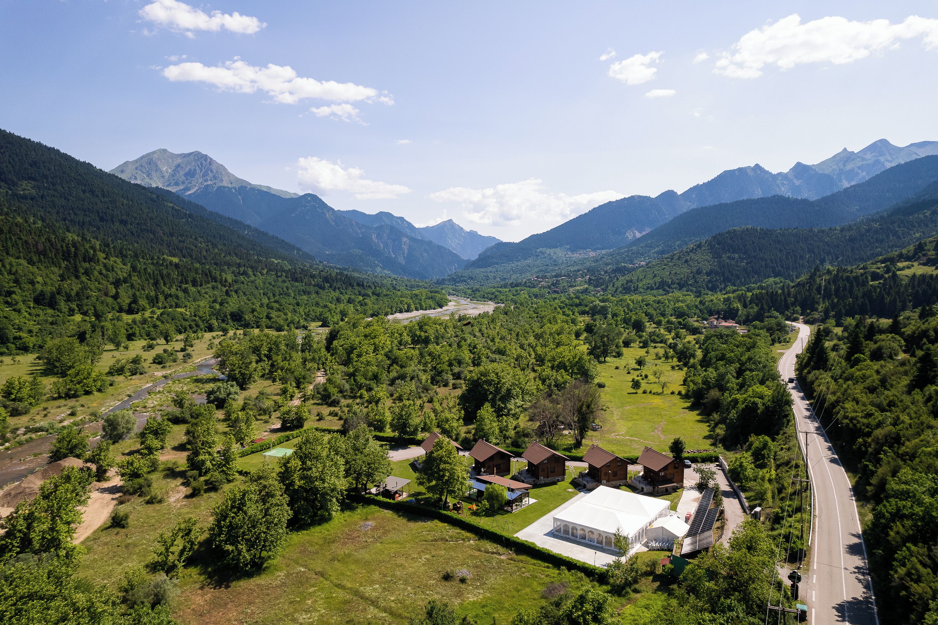 Paesaggio montano rurale con una strada, case e un grande edificio bianco.