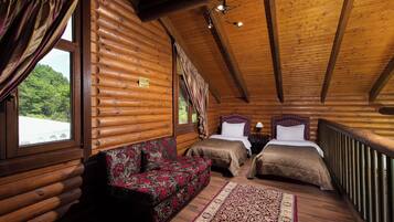 A log cabin bedroom with two beds, a sofa, and a view of a forest.