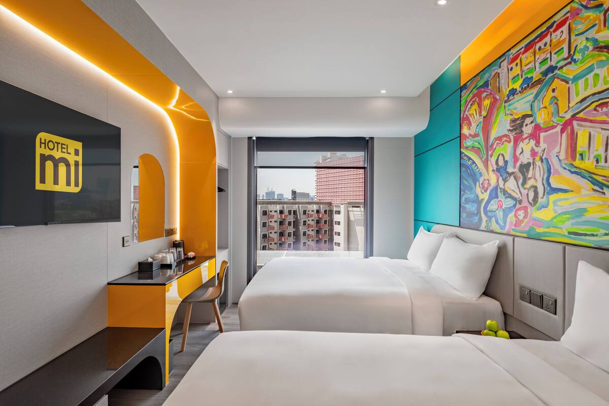 A modern hotel room with a large bed, a desk, and a view of the cityscape.