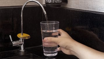 Una mano llenando un vaso con agua de un grifo moderno.