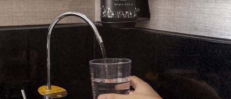 Una mano llenando un vaso con agua de un grifo moderno.