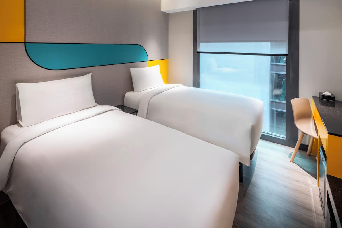 A hotel room with two beds, a desk, and a window with a view.