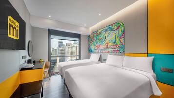 A hotel room with two beds, a large window with a city view, a colorful abstract painting on the wall, and a minibar.
