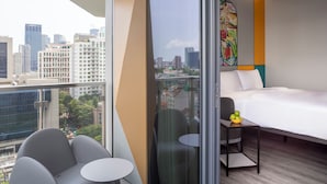 Habitación de hotel moderna con vista a la ciudad, una cama, una mesita con un cuenco de fruta y un par de sillas.